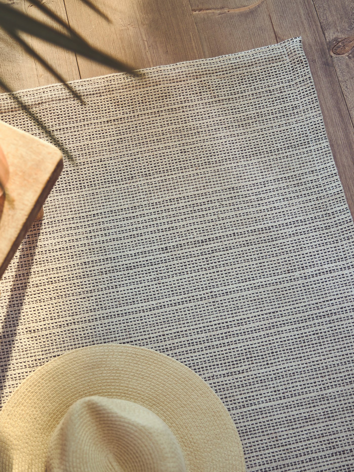 Detalle de una alfombra moderna hecha de algodón reciclado en el suelo del salón, junto a un sombrero y una planta. 
