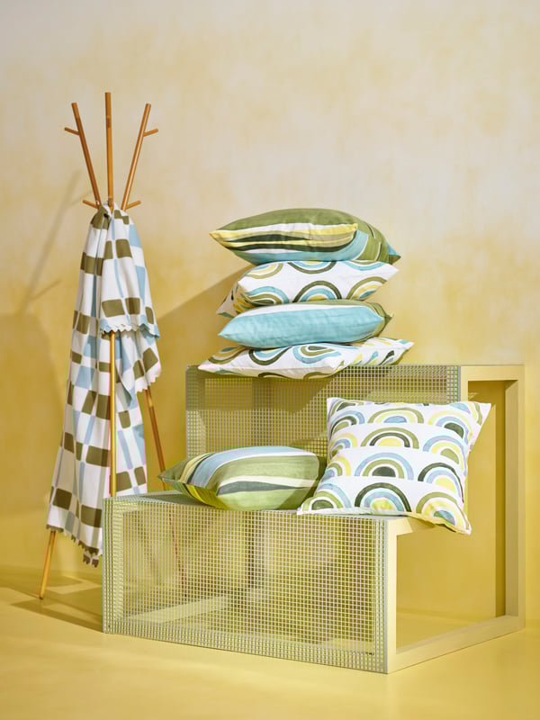 Image consisting of various elements against a yellow background: cushions, hat and coat stand and blanket with geometric patterns.