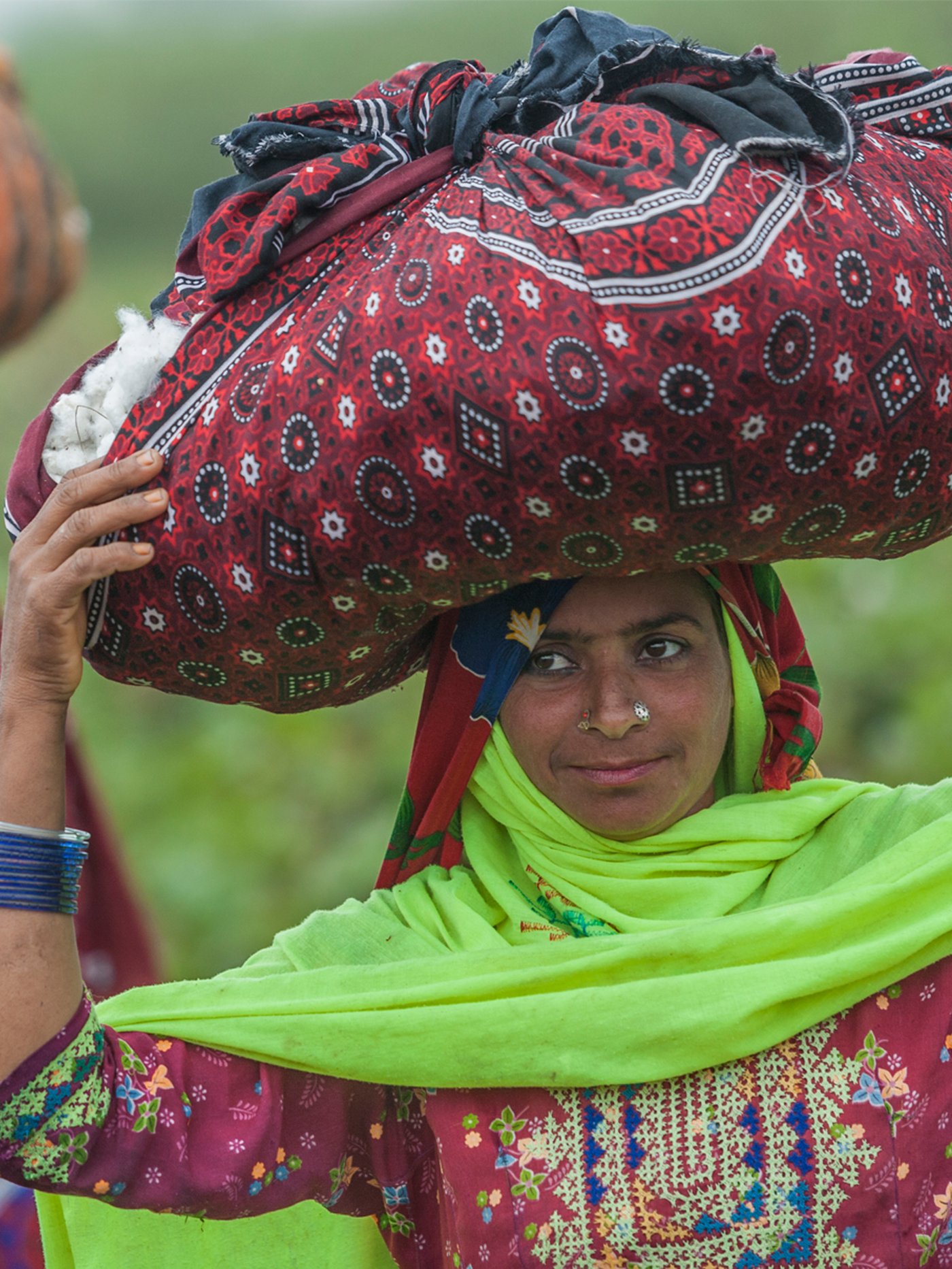 A cotton picker dressed in brightly coloured clothes carrying a bundle of picked cotton wrapped in a large cloth.