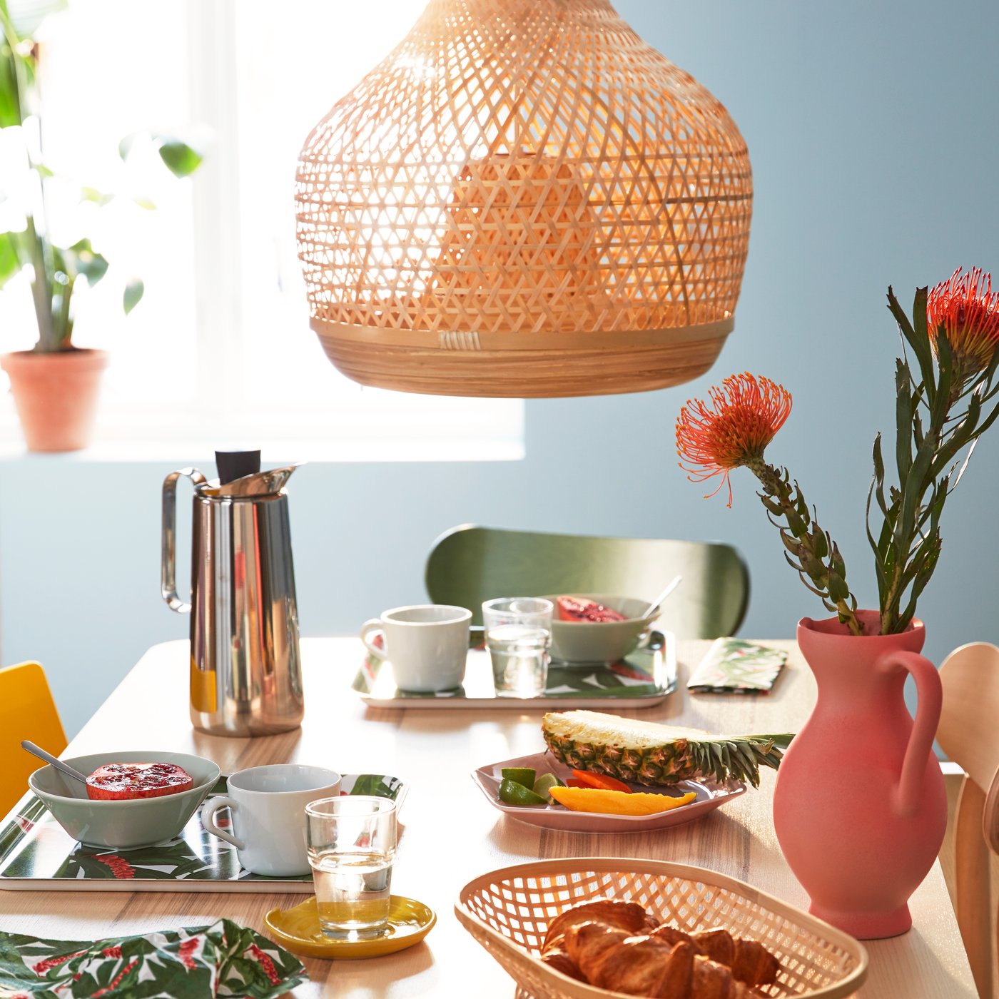 Lámpara de techo sobre una mesa con platos, termo, florero rosado y comida.