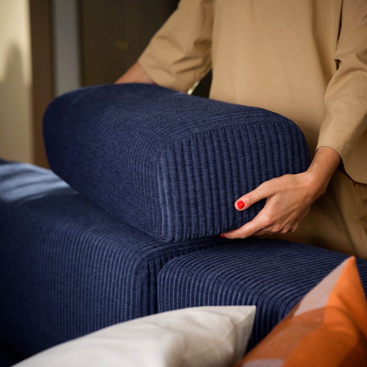 A person standing by a dark-blue JÄTTEBO four-seat modular sofa places a loose headrest on top of the backrest.