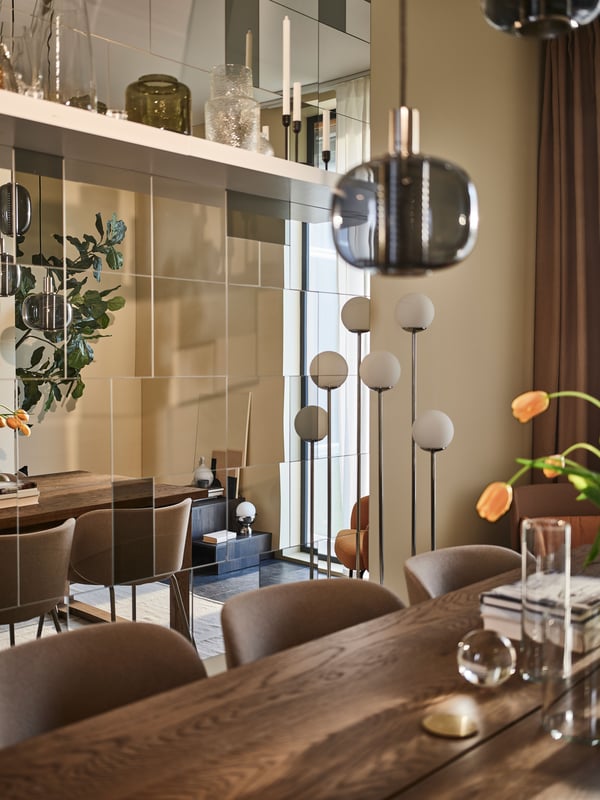 An elegant dining room with a MÖRBYLÅNGA table, KRYLBO chairs, and a statement wall made up of several BLODLÖNN mirrors.