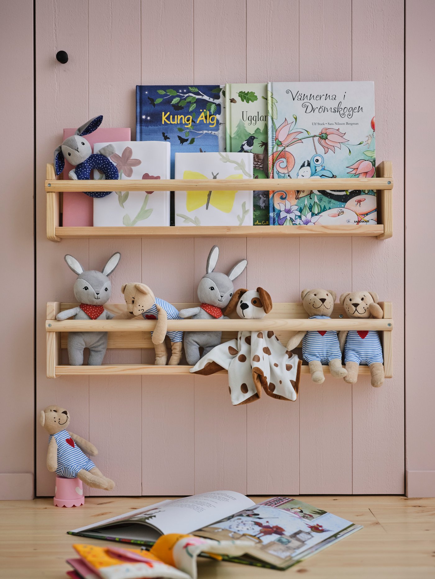 Twee FLISAT wandrekken boven elkaar aan de muur, gevuld met hardback boeken en zachte knuffels, waaronder een FABLER BJÖRN knuffelbeer.