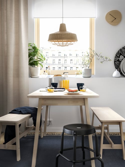 A dining spot next to a window with a birch NORRÅKER dining table, two benches, a black stool and a blue rug.