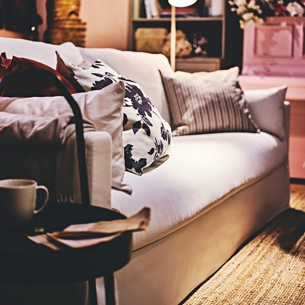 Biała sofa HYLTARP, na której leżą czarna i czerowna poduszka dekoracyjna.