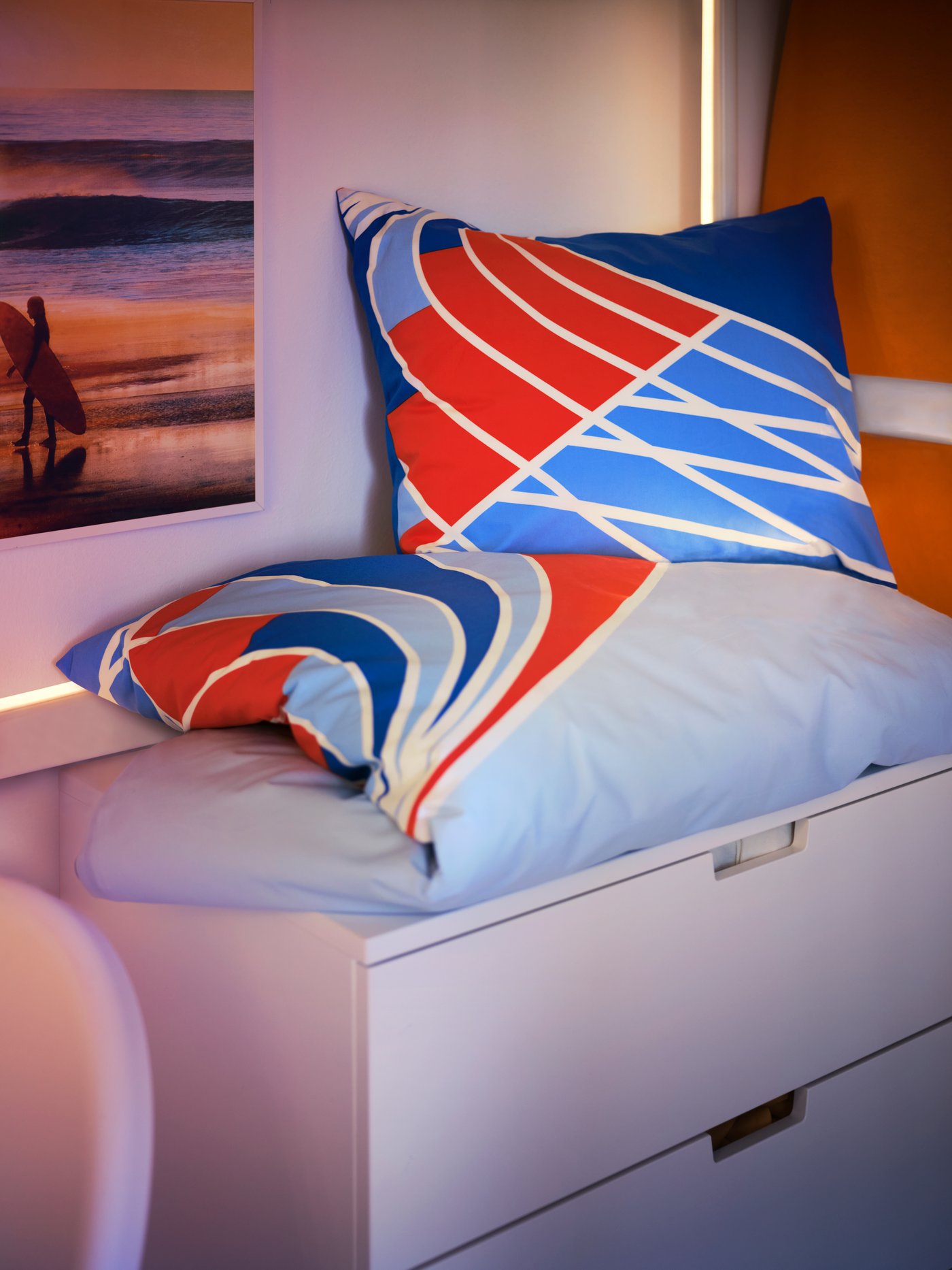 A SPORTSLIG quilt cover and pillowcase with a running track pattern in red, white and blue on a NORDLI chest of drawers.