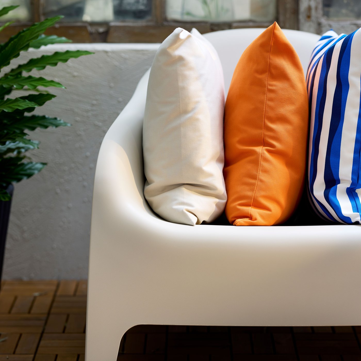 A white SKARPÖ outdoor armchair and three cushions with white, orange and blue-and-white striped cushion covers.