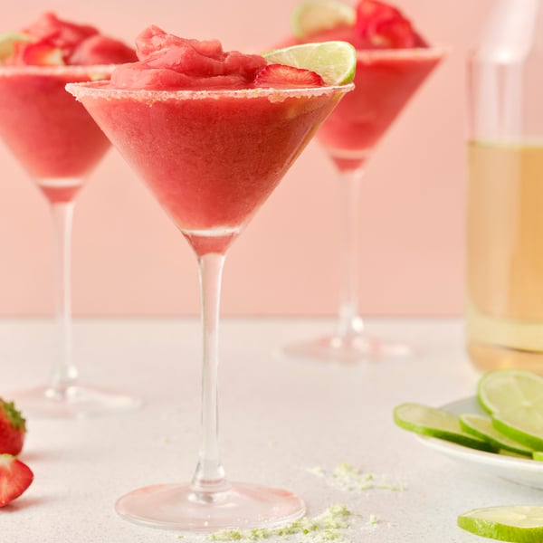 Tři vysoké sklenice s margaritami ze syceného nealkoholického nápoje ISKUB s příchutí bezového květu a mražených jahod, ozdobené limetkou.
