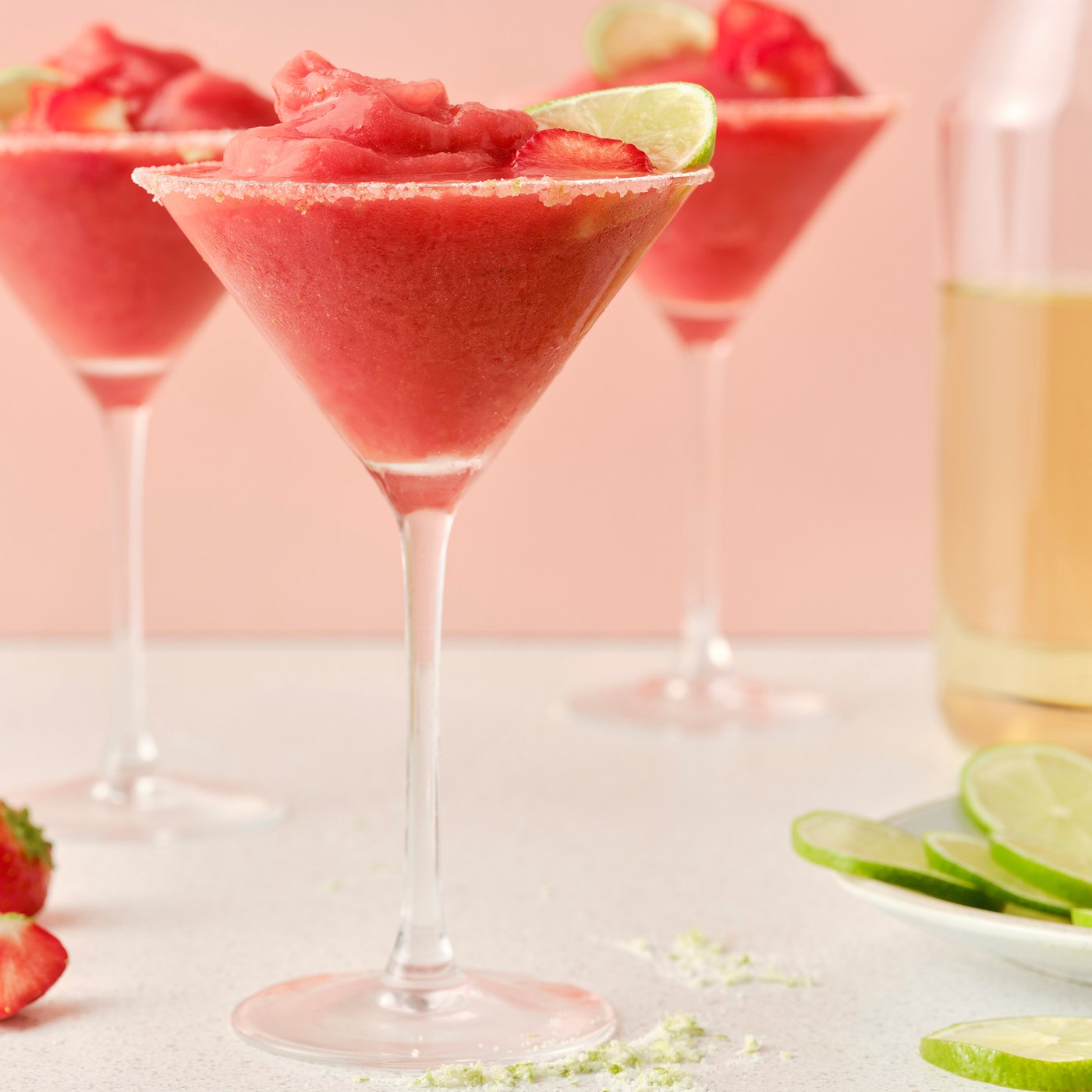 Three tall glasses filled with ISKUB elderflower soft drink and frozen strawberry margaritas, garnished with lime.