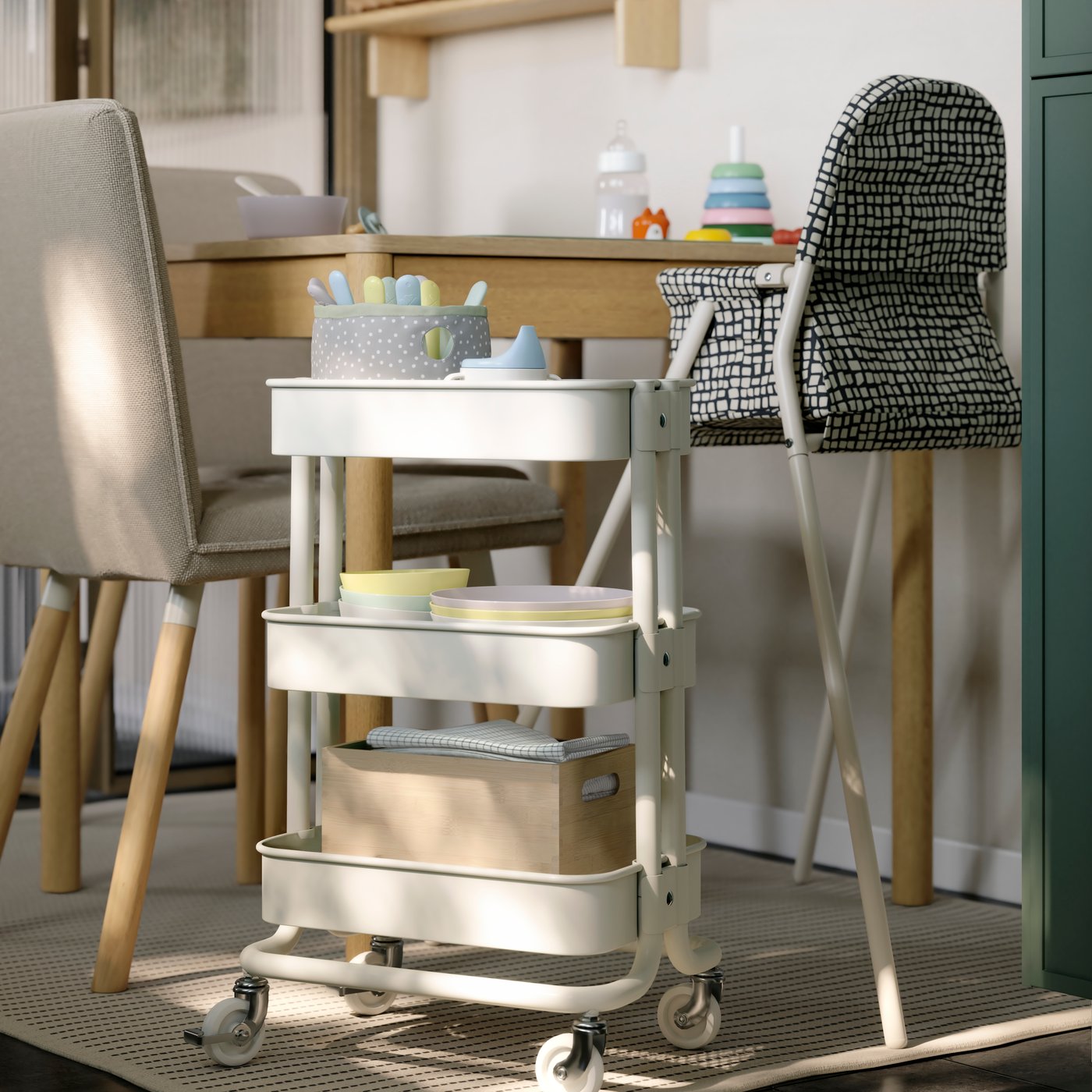 A white RÅSKOG trolley is placed next to a TONSTAD extendable table. It has baby-related items stored on the mesh shelves.