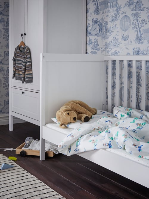 A white SUNDVIK cot with a side removed for a three-walled bed with blue and white bedding and a soft toy do by a wardrobe.