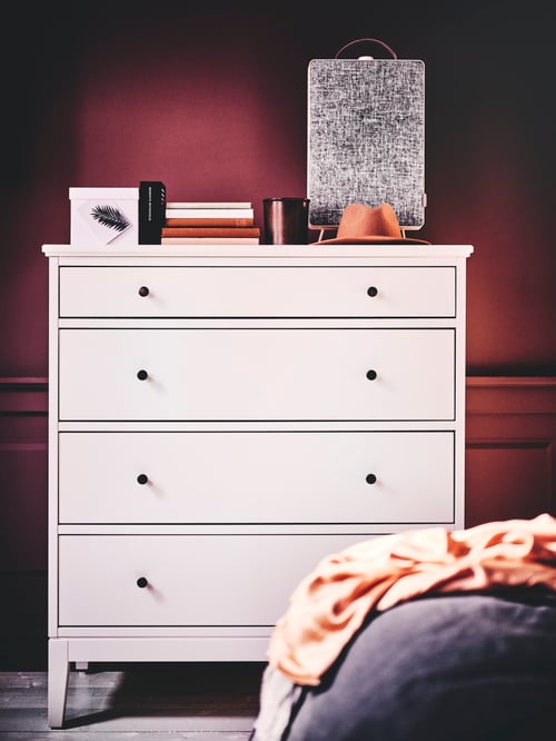 Close-up on bedroom with rectangular white wooden chest of 4 drawers with one small drawer, holding books and air purifier.