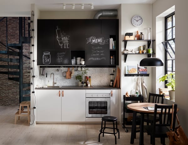 A small kitchen corner with white cabinets at the bottom and chalk doors inscribed with messages above.