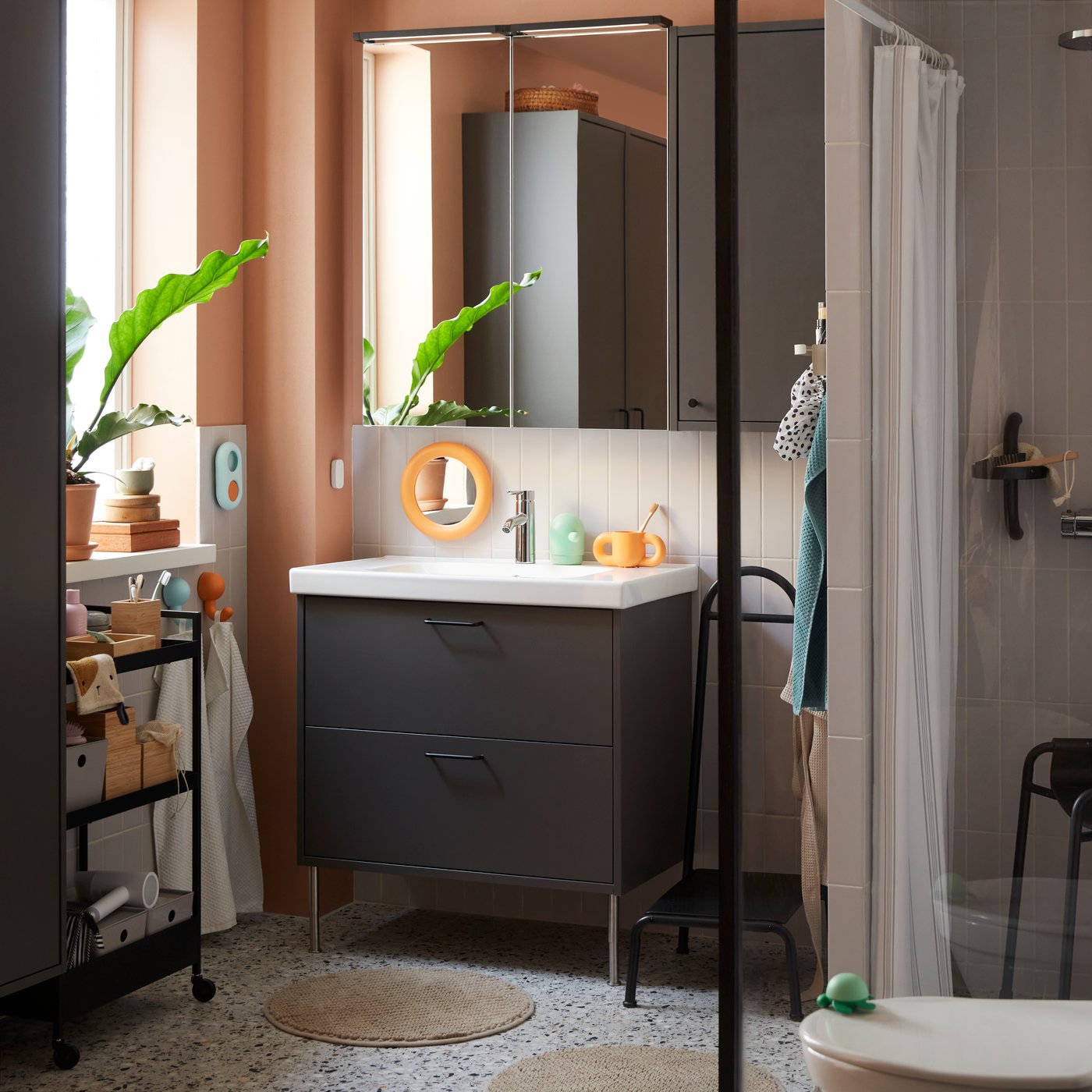 A bathroom featuring a dark grey HAVBÄCK wash stand with drawers, a basin, and tap, alongside mirrors and bathroom interior.