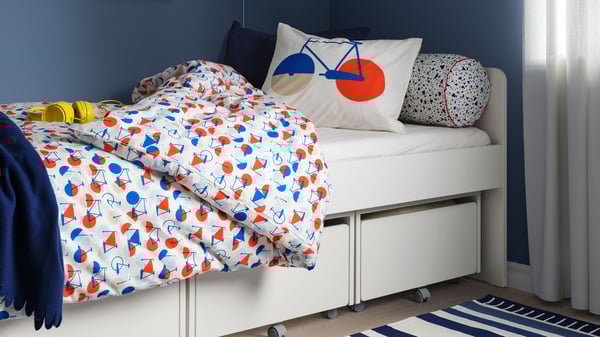 Una cama SLÄKT con tres cajones blancos. La ropa de cama tiene patrones de bicicletas.