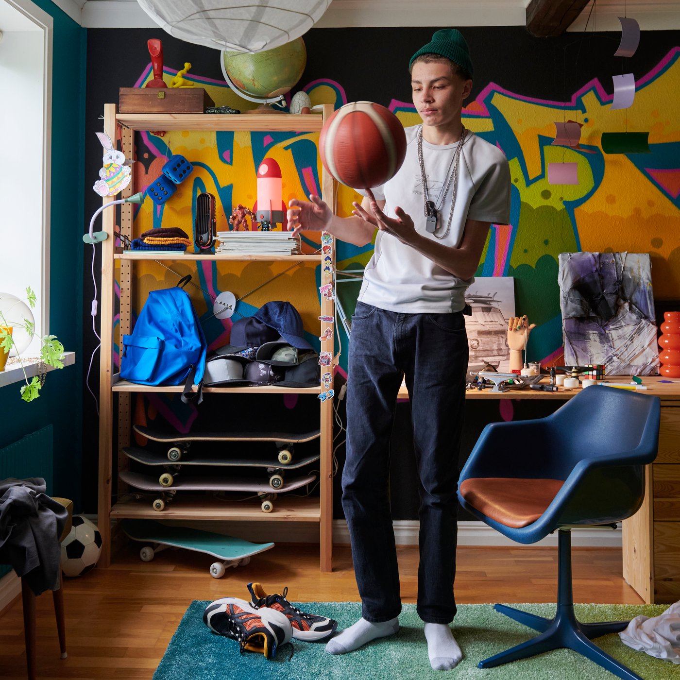 Nastolatek z piłką do koszykówki w ręce stoi w swoim pokoju na tle sosnowego regału IVAR.