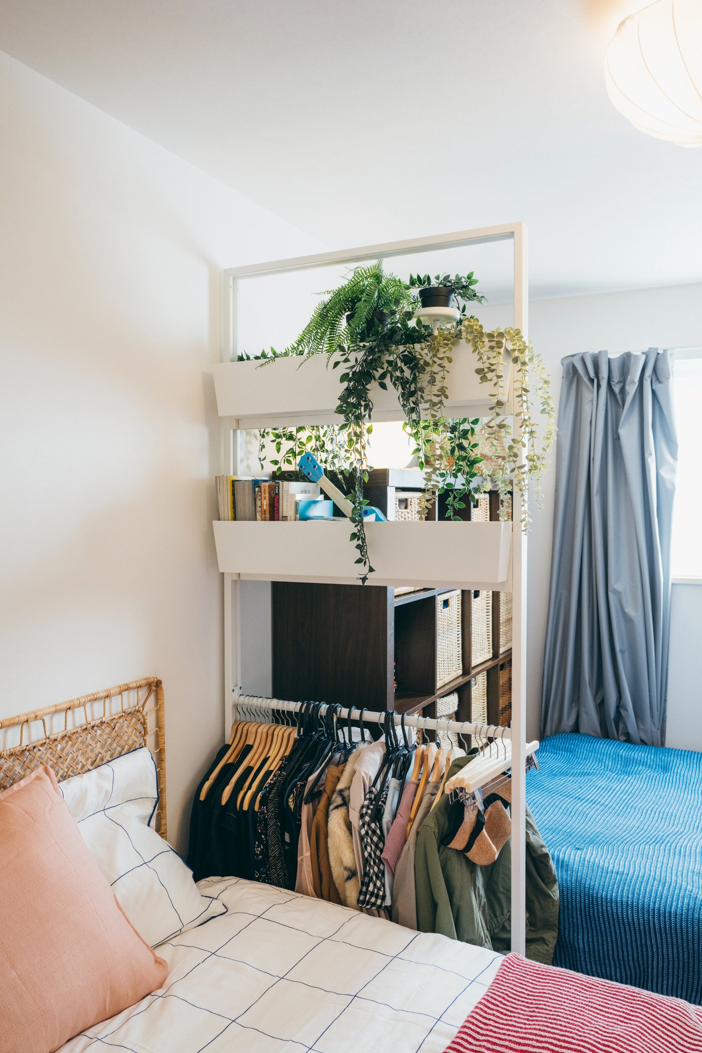 ベッドの間に置かれた収納ラックに洋服がかけられ、観葉植物が置かれている。