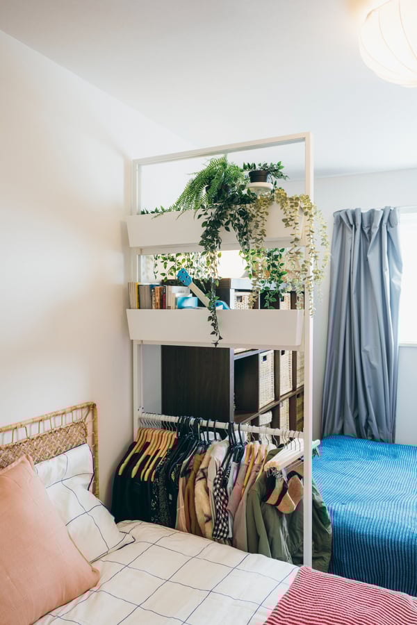 2つのベッドの間の白いラックに洋服と観葉植物が置かれている。