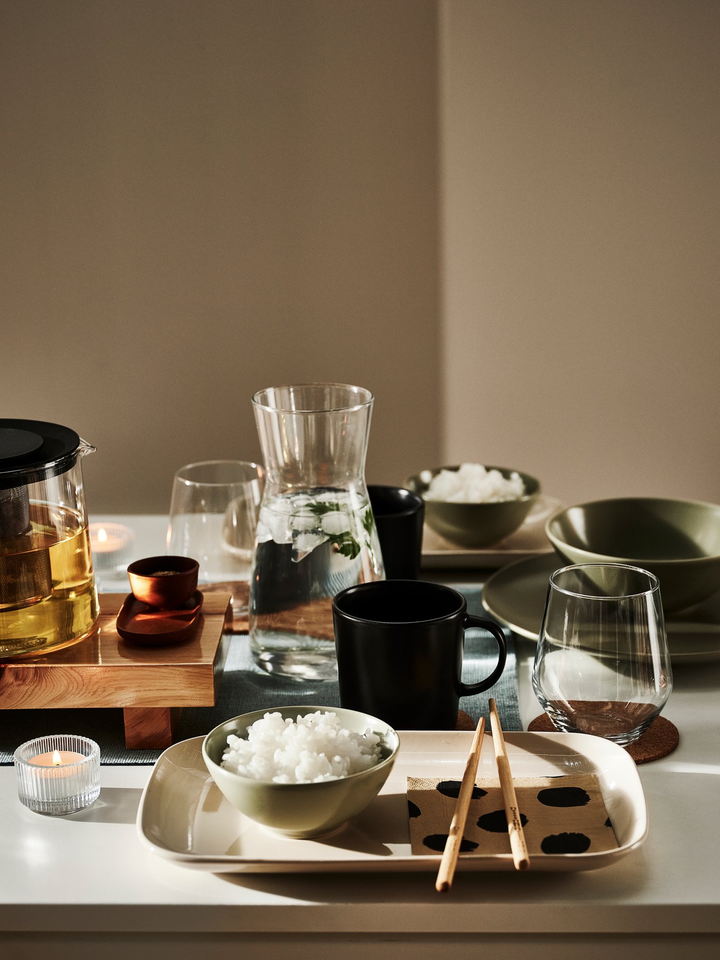 Un comedor moderno con una jarra, una taza, bowls verdes, platos rectangulares y varios vasos.