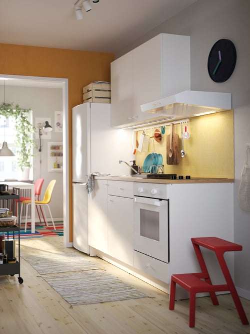Kitchen with white KNOXHULT cabinets with doors and drawers, with two rugs and a red step stool on a wooden floor.