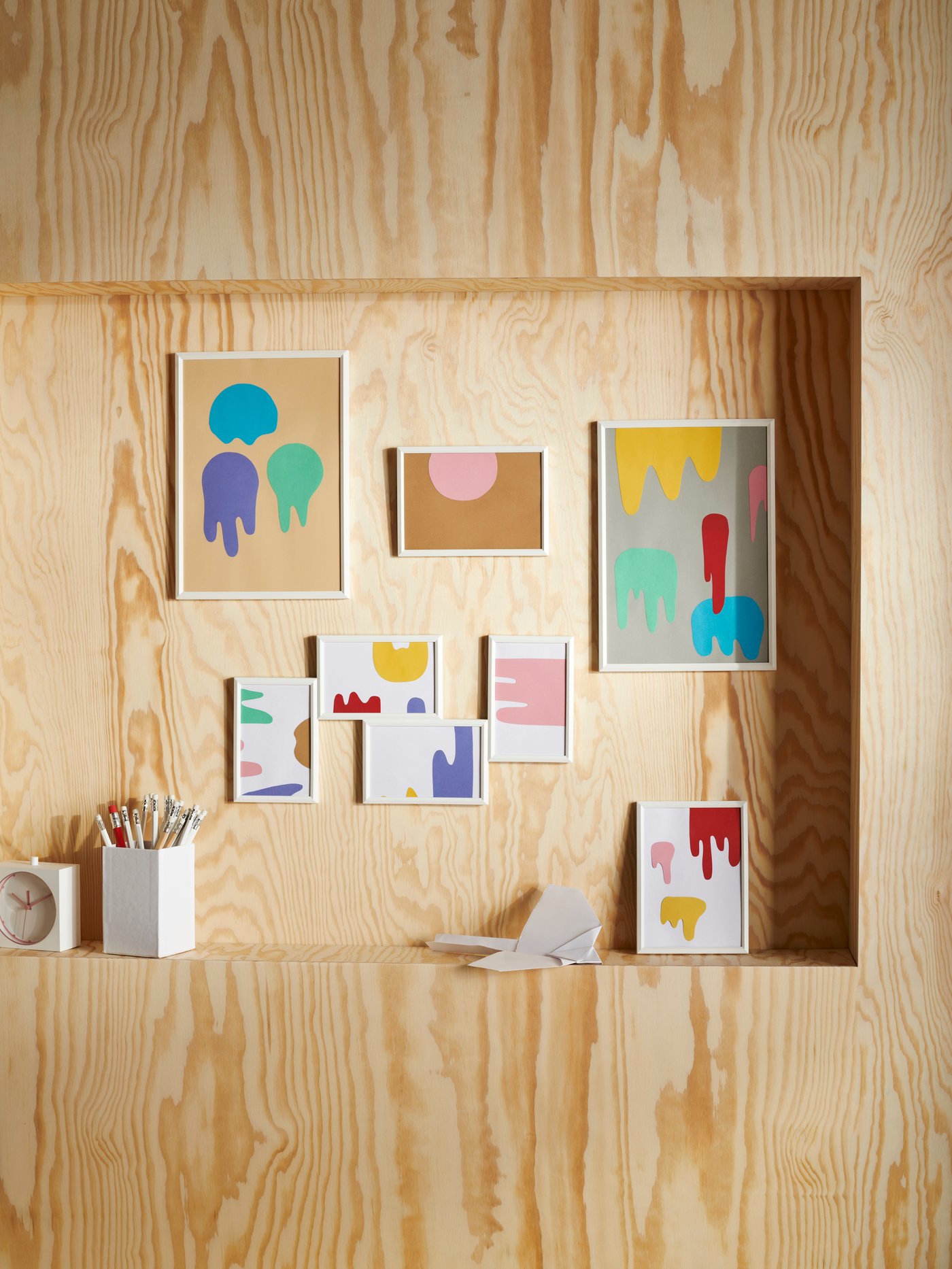 Una serie de marcos YLLEVAD blancos de varios tamaños con diseños de salpicaduras de pintura en una pared de madera contrachapada.