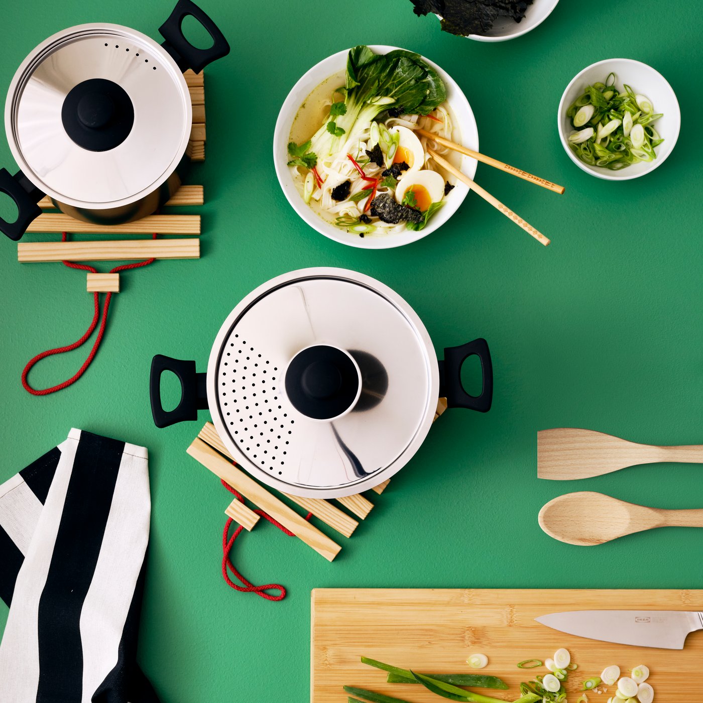 Une planche à découper APTITLIG en bambou, un faitout avec couvercle HEMLAGAD ainsi qu’une assiette creuse et un bol IKEA 365+ contenant de la nourriture.