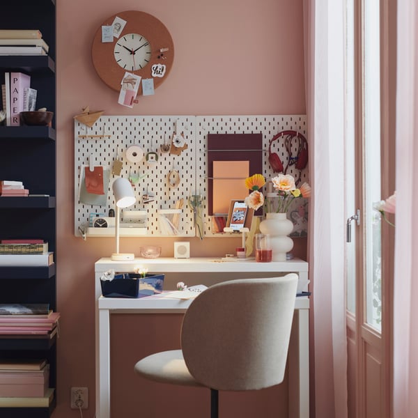 Une chaise pivotante KRYLBO est placée devant un bureau. Au mur, au-dessus, se trouvent des panneaux perforés SKÅDIS et une horloge murale SVARTGÖK.