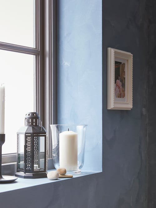 Deep windowsill with an ENRUM lantern, a glass vase with candle, candlestick and stones, plus picture frame on the wall.