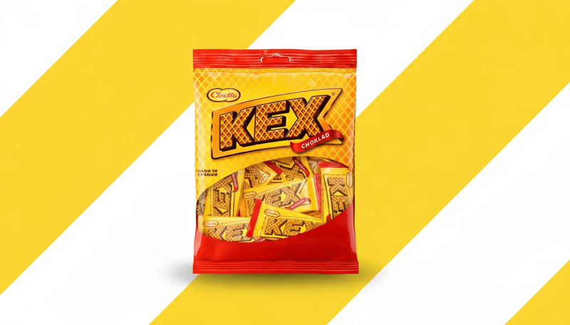 Zak Kex chocoladekoekjes van Cloetta op een achtergrond met brede gele en witte diagonale strepen, centraal weergegeven in een promotionele setting.