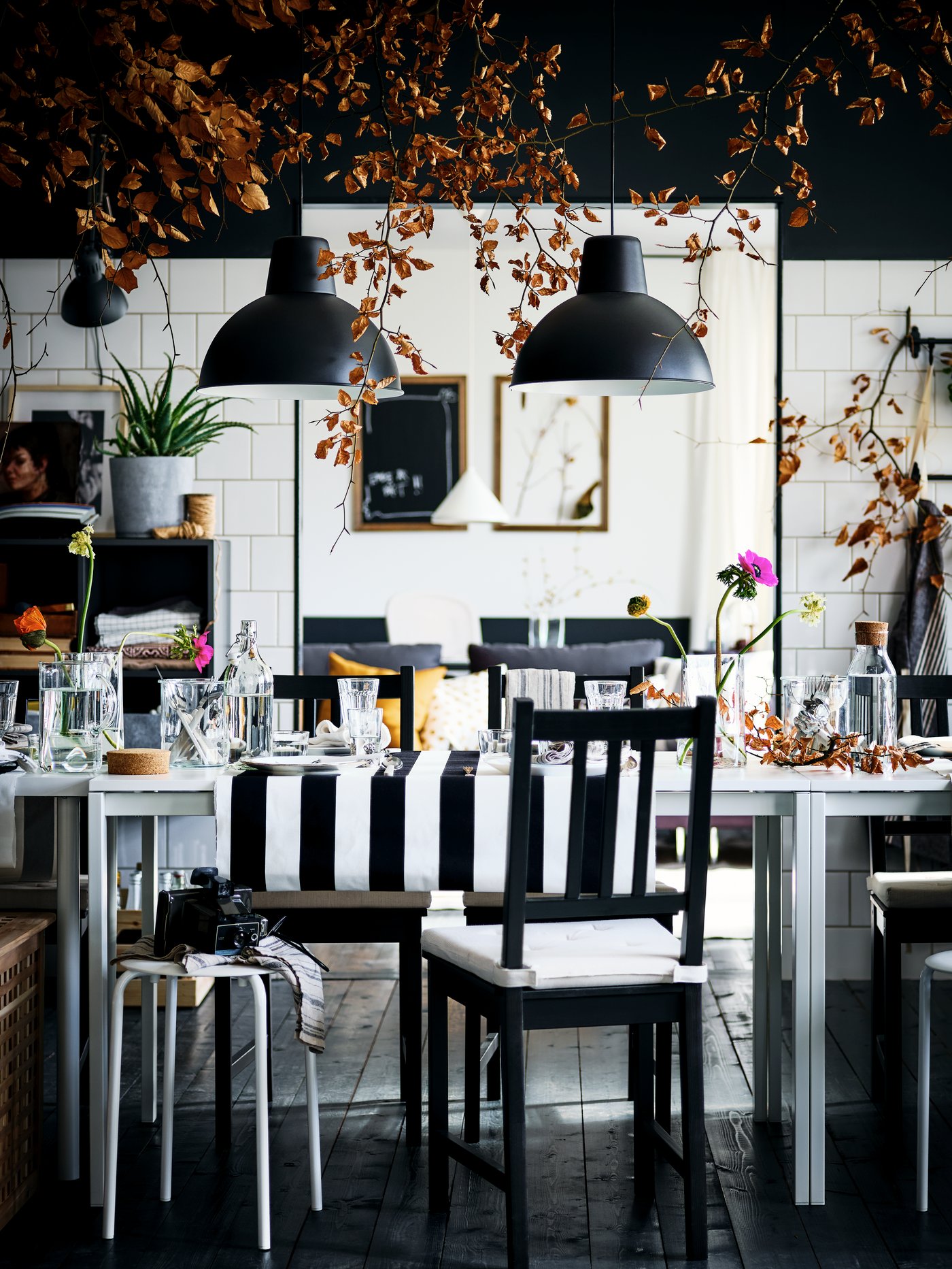 A decked-out dining area with brown-black STEFAN chairs round two white MELLTORP tables. Black SKURUP pendants hang above.