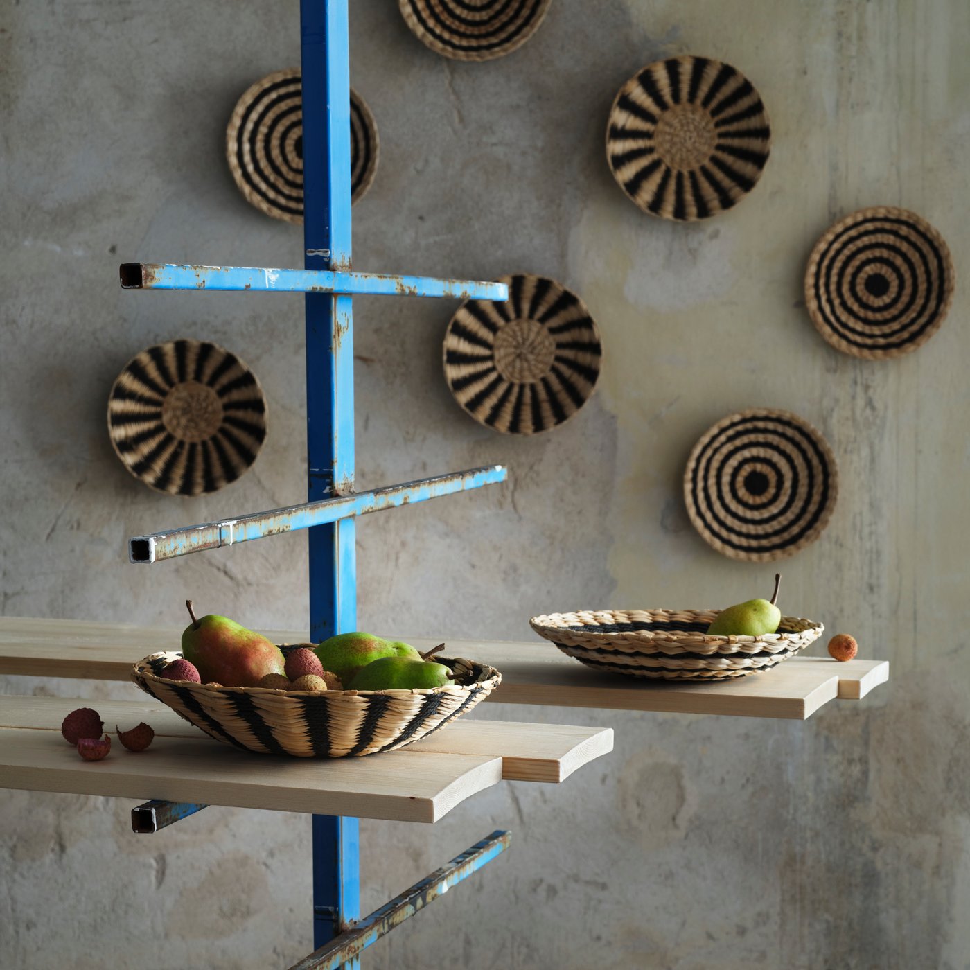 Five MÄVINN wall decoration hang on a grey wall. In front of them are two wall decorations used as bowls of fruit.