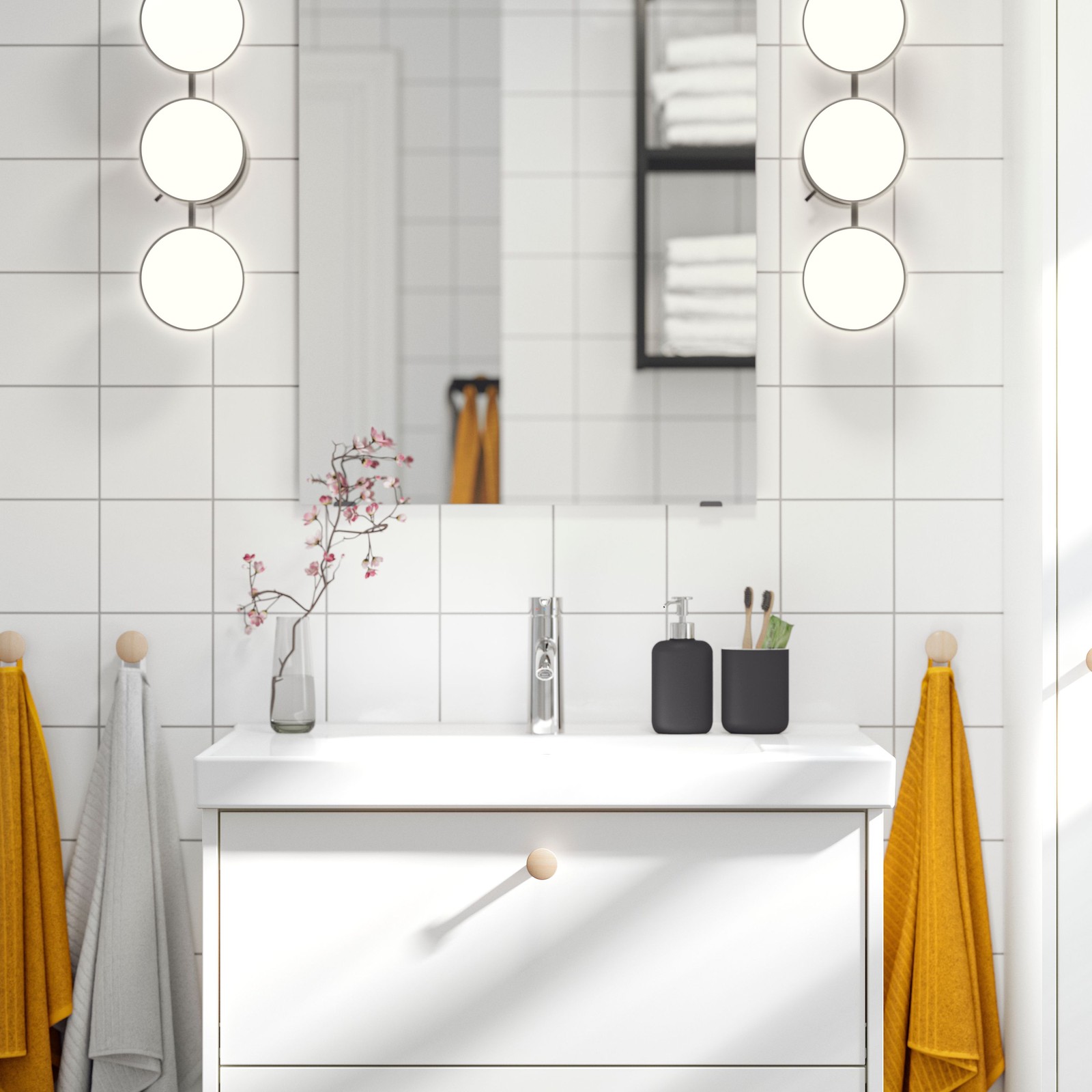 A white-tiled bathroom has a white HAVBÄCK wash-stand with a square mirror above it and two lit lamps on either side.