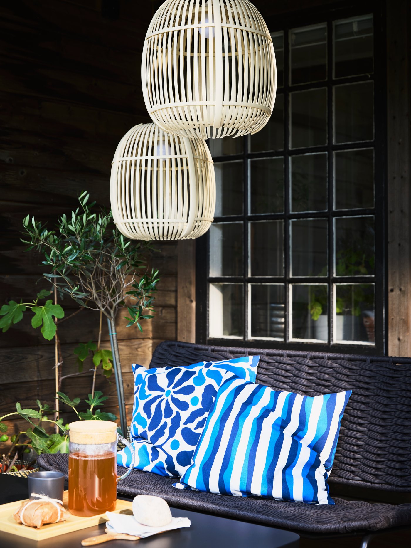 TEGELÖN black sofa with blue and white pillows, a table set with a 365+ carafe of tea, and decorative lighting above.