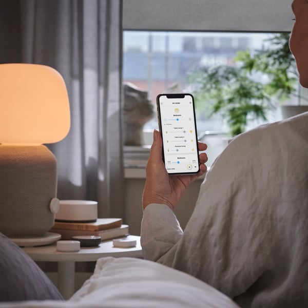 A hand is holding a mobile phone up to look at the screen. A smart light is turned on beside.