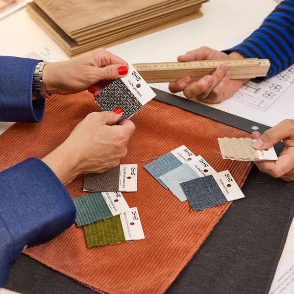 Two people comparing fabric samples and swatches on a table while discussing design options and using a ruler for measurement.