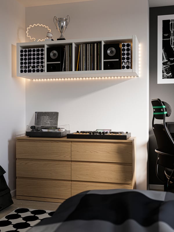 Cassettiera MALM in rovere chiaro su cui sono appoggiati dei giradischi. Fissato alla parete, sopra la cassettiera, c'è uno scaffale KALLAX bianco.