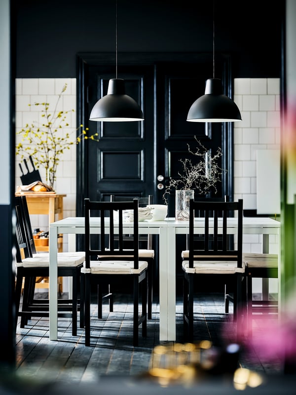 A black-and-white dining area, two white MELLTORP tables, brown-black STEFAN chairs, white wall tiles and a dark-wood floor.