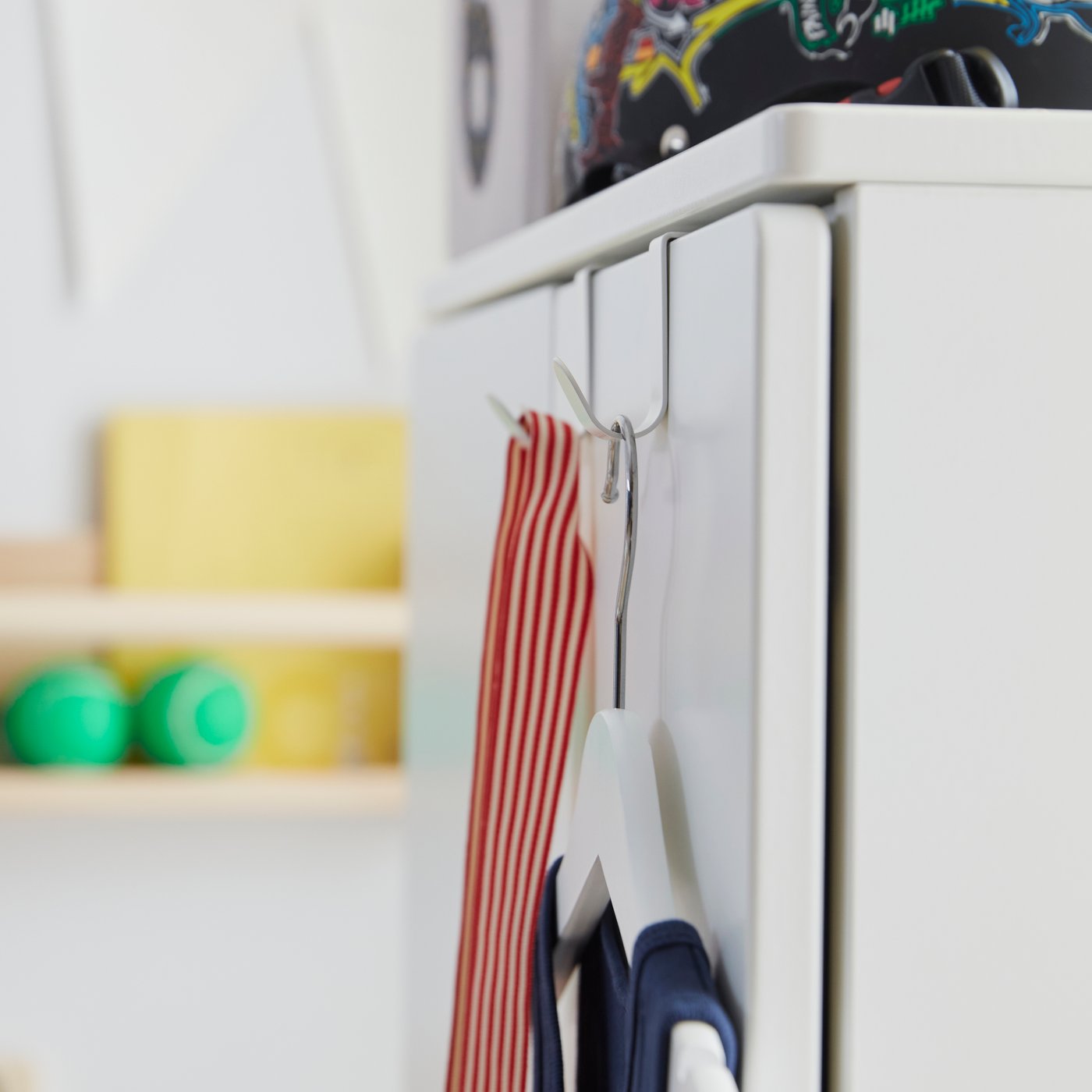 The white LÄTTHET hooks used on the exterior of SMÅSTAD storage for hanging clothes in a colourful children’s room.
