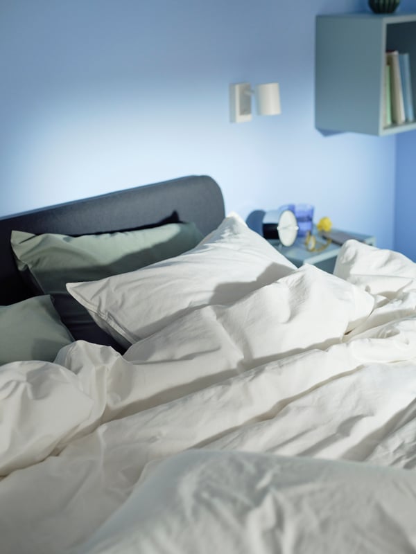 Lit matelassé SLATTUM gris foncé avec linge de lit ÄNGSLILJA blanc contre un mur avec applique/liseuse NYMÅNE.