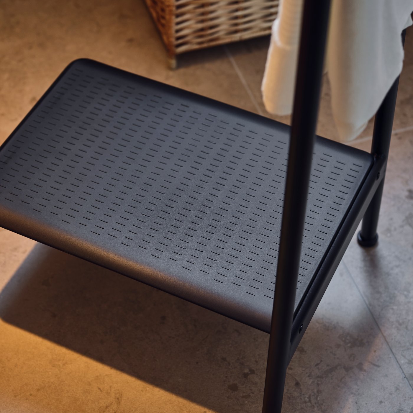 A closeup of a dark grey BÄSINGEN step stool with handrail, showing the small holes for draining water and prevent slipping.