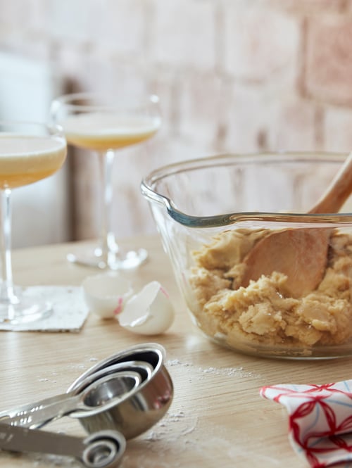 O poză de aproape cu două pahare de șampanie care conțineau lichid, o ceașcă de măsurare, un bol cu amestec de alimente și coji de ouă.