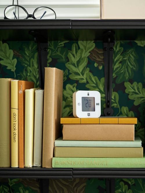 Modern bedroom with a wall shelf with books, a pair of glasses an alarm clock and wall with a leaf pattern design.