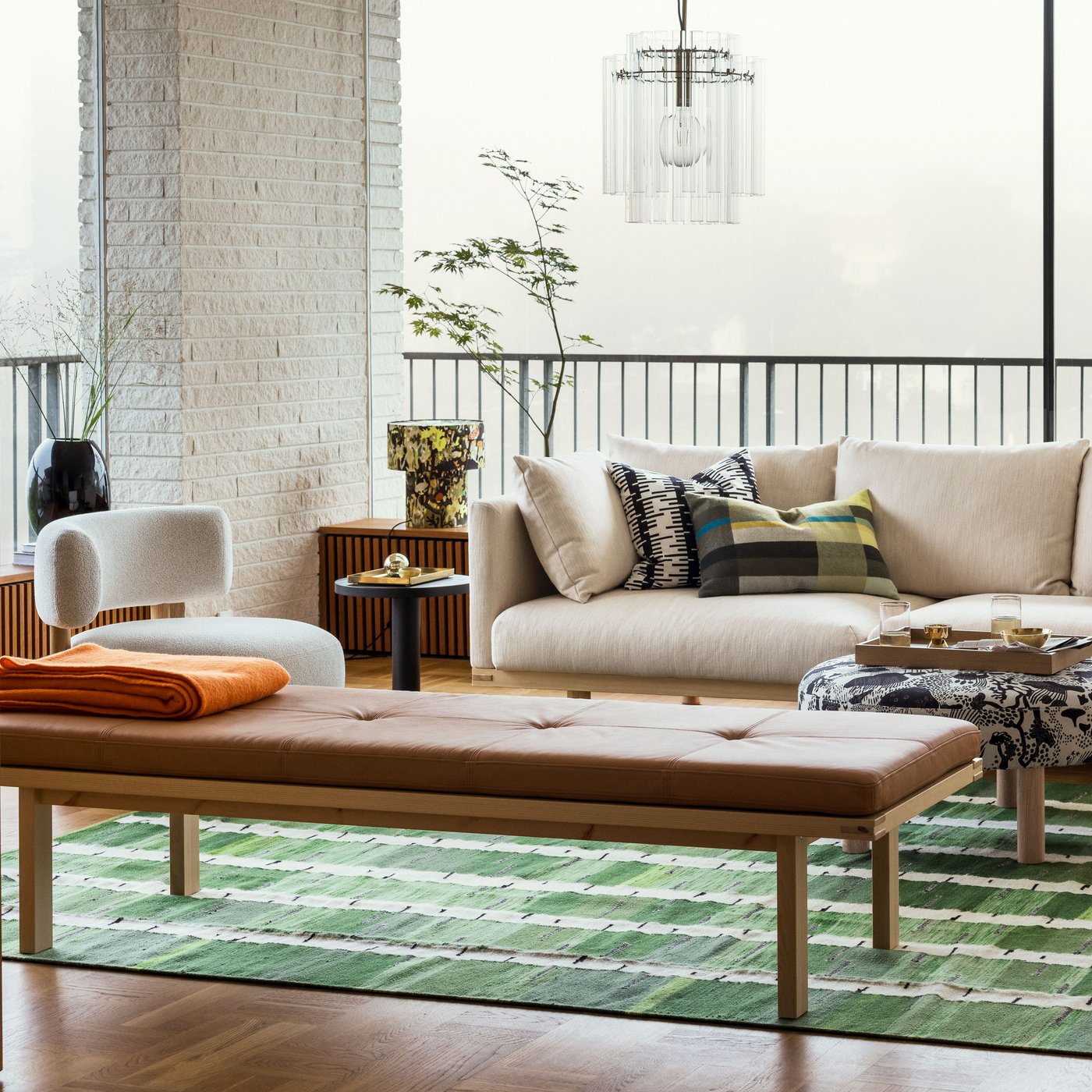 A bright living room with a beige STOCKHOLM 2025 3-seat sofa by a bench and pouffe sitting on a green, black, and white rug.