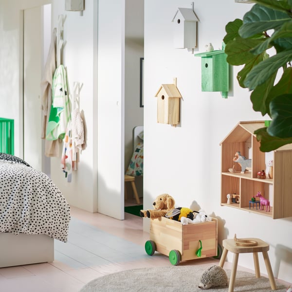 A wood FLISAT toy storage with wheels and a FLISAT children’s stool by a FLISAT doll’s house shelf on the wall above.