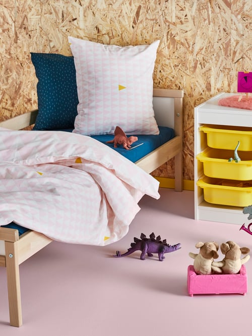 Children room with a bed frame and guard rail, with two pillows and a duvet, and a storage combination with boxes.