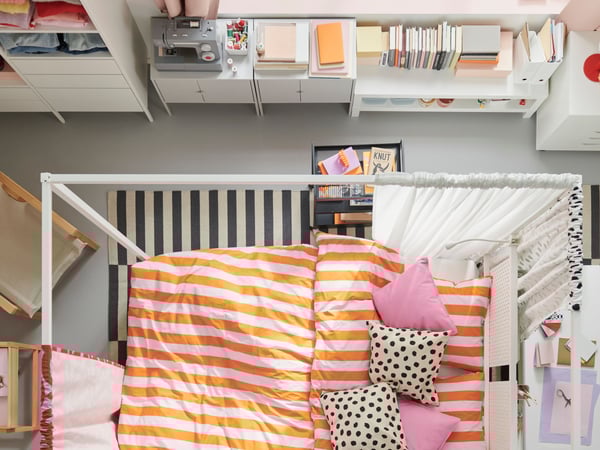 A bird’s eye view of a colourful bedroom. A white VITARNA four poster bed is in the centre, covered in SLÅNHÖSTMAL bed linen.
