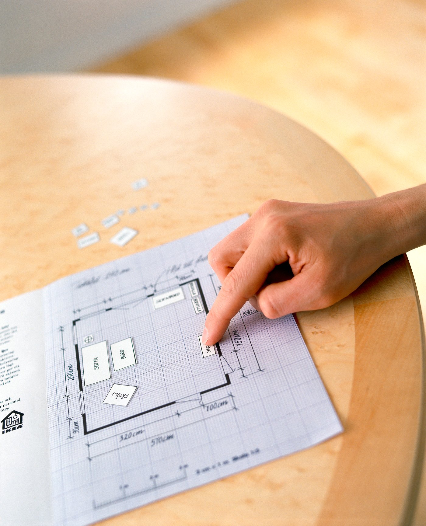 Ruka uspořádává nákresy nábytku v půdorysu místnosti.