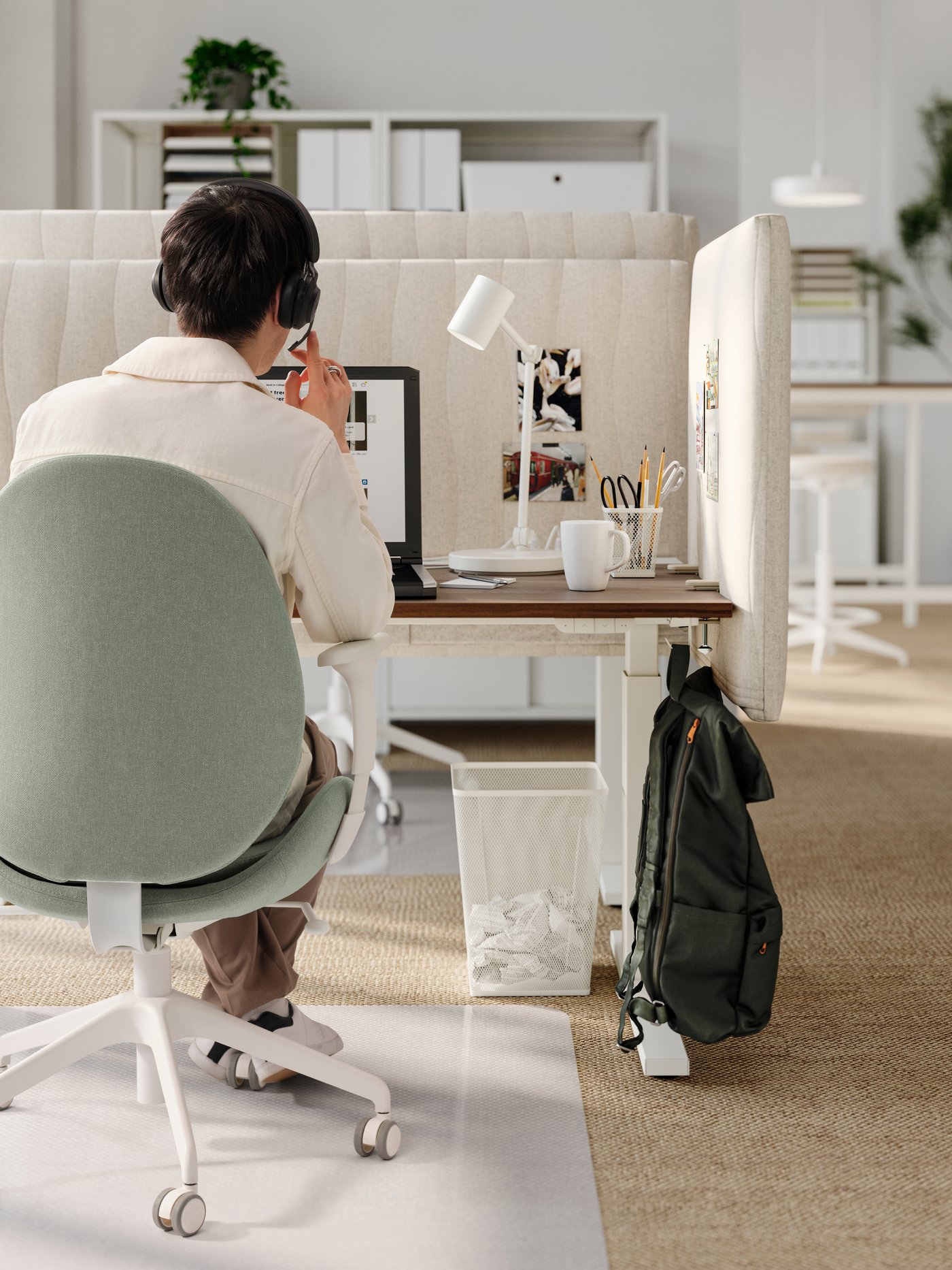 A man with a headset sitting in a green GRÖNFJÄLL office chair at a walnut/white desk with MITTZON acoustic screens for desk.