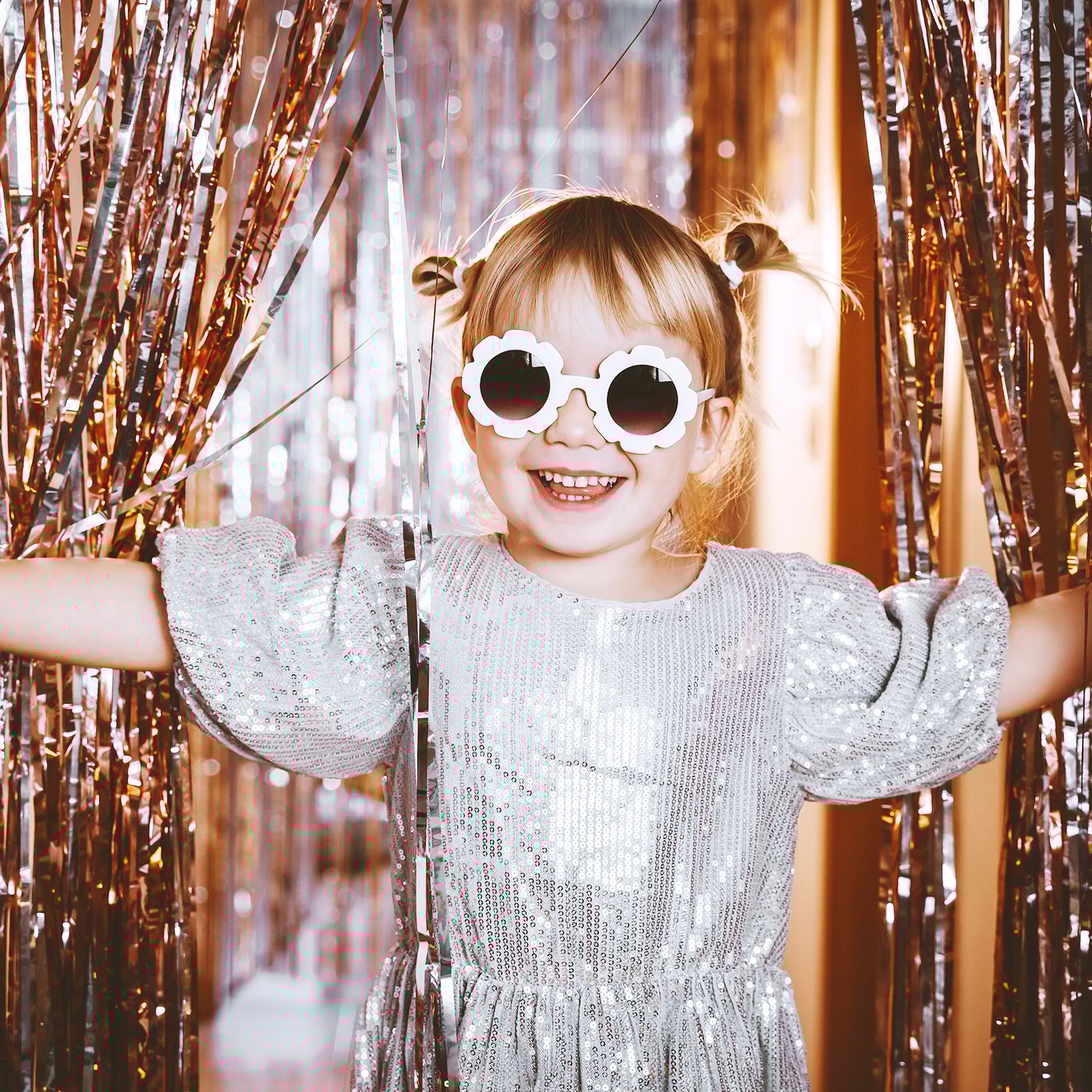 A little girl with sunglasses walking through a confetti curtain.