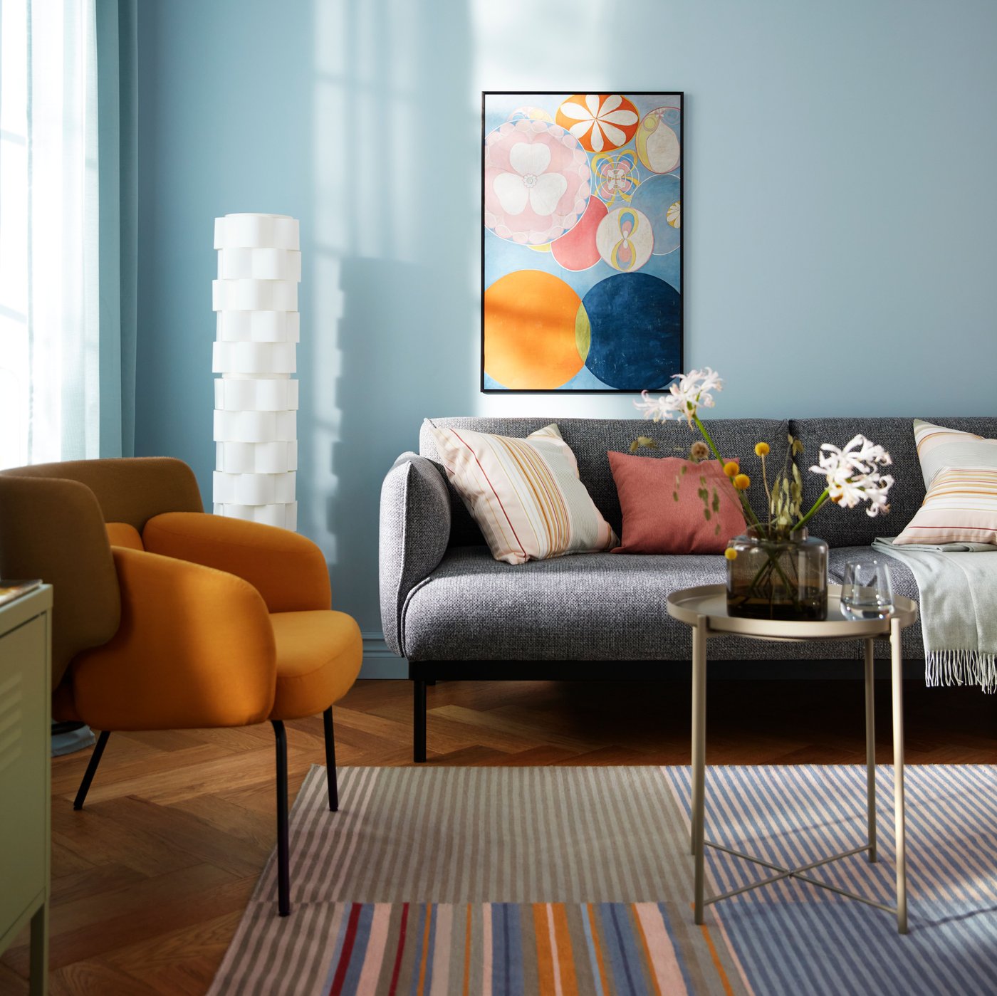 A colourful yet sparsely furnished living room with a single art piece in a black LOMVIKEN frame on a light-blue wall.